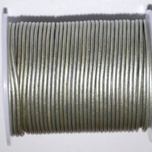 Puede incluir: Un carrete de cordón de cuero plateado. El cordón está enrollado firmemente alrededor del carrete y está listo para ser utilizado en proyectos de artesanía.