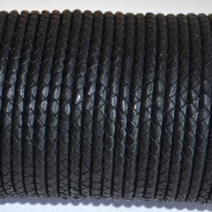 Puede incluir: Un rollo enrollado de cord&oacute;n de cuero trenzado negro. El cord&oacute;n est&aacute; hecho de muchos hilos entrelazados, creando una superficie texturizada. El color oscuro y el dise&ntilde;o trenzado sugieren un material duradero adecuado para varios proyectos de artesan&iacute;a.