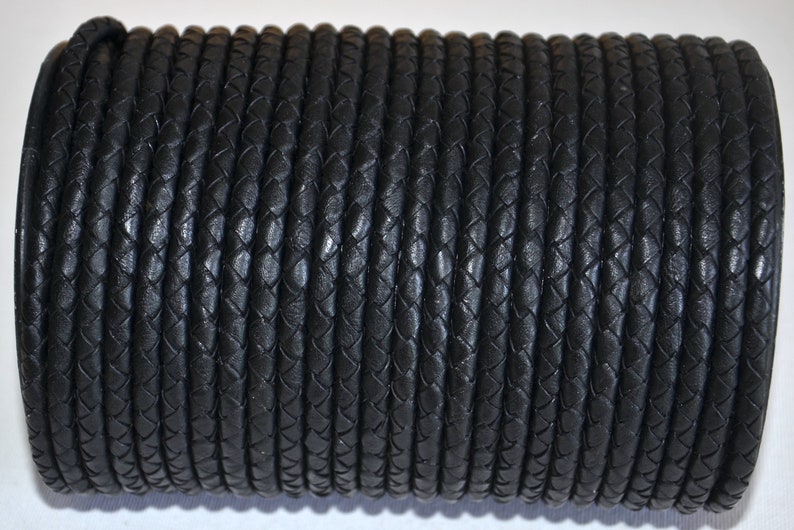 Puede incluir: Un rollo enrollado de cord&oacute;n de cuero trenzado negro. El cord&oacute;n est&aacute; hecho de muchos hilos entrelazados, creando una superficie texturizada. El color oscuro y el dise&ntilde;o trenzado sugieren un material duradero adecuado para varios proyectos de artesan&iacute;a.