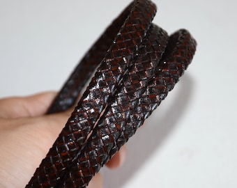 Può includere: Cavo in pelle intrecciata di colore marrone scuro. Il cavo è intrecciato fittamente, creando una superficie strutturata. Il cavo è flessibile e sembra essere lungo diversi metri.