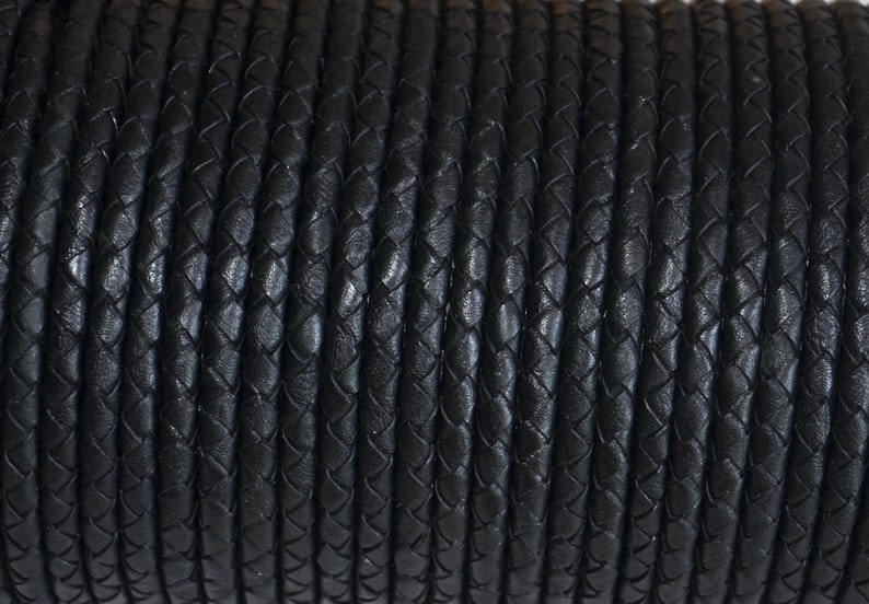 Puede incluir: Primer plano de un carrete de cord&oacute;n de cuero trenzado negro. El cord&oacute;n est&aacute; tejido apretadamente, creando una superficie texturizada. El color oscuro y el trenzado detallado sugieren un material duradero adecuado para varios proyectos de artesan&iacute;a.
