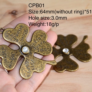 May include: Two antique gold-tone four-leaf clover charms with a clear rhinestone in the center. Each charm has different words inscribed on each leaf: "Amore", "Macal", "Good Luck", "Cherse Anno Bonne Chance", "Suerite", "Buena", "Certo A", and "Good Luck".