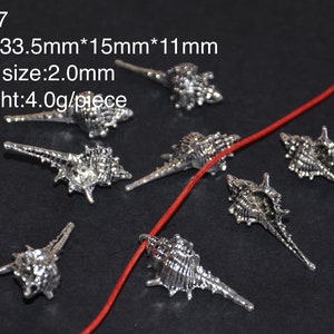 May include: Silver-toned seashell charms with a detailed design. The charms are approximately 3.35 inches long, 1.5 inches wide, and 1.1 inches tall. Each charm has a 2.0 mm hole for stringing.