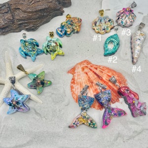 May include: A collection of ocean-themed pendants featuring sea turtles, starfish, mermaid tails, and various seashells. Each piece is crafted with colorful glitter and resin, finished with a metal bail. Labels #1, #2, #3, and #4 identify specific shells.