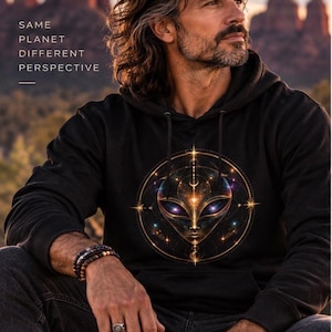 May include: A black hooded sweatshirt featuring a graphic of an alien face centered within a golden circular geometric design. The text SAME PLANET DIFFERENT PERSPECTIVE is printed in white on the upper left side of the chest area.