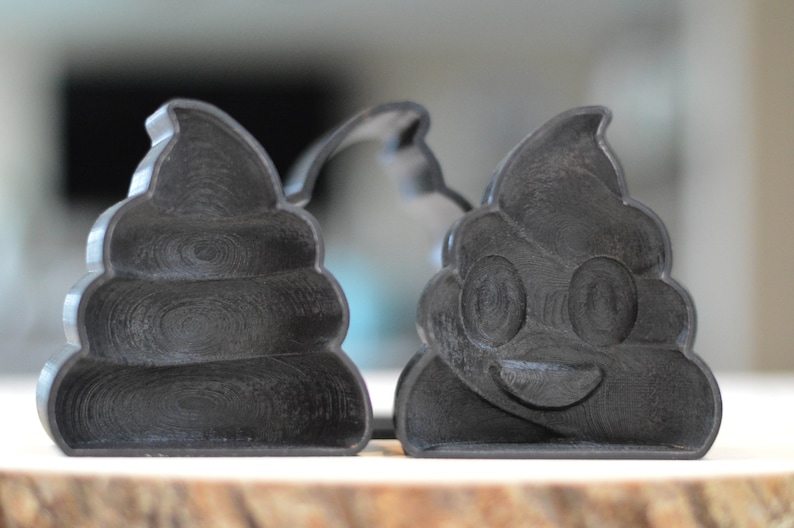 Puede incluir: Dos cortadores de galletas impresos en 3D en negro con forma de pila de caca. Un cortador tiene una cara sonriente con ojos y boca.