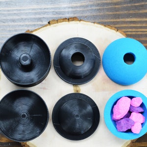 May include: Six round, black and blue containers with lids. The lids are all different shapes and sizes. Some of the containers are filled with pink and purple candy.