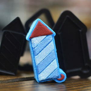May include: A blue and white striped firework with a red top, surrounded by black and grey firework moulds.