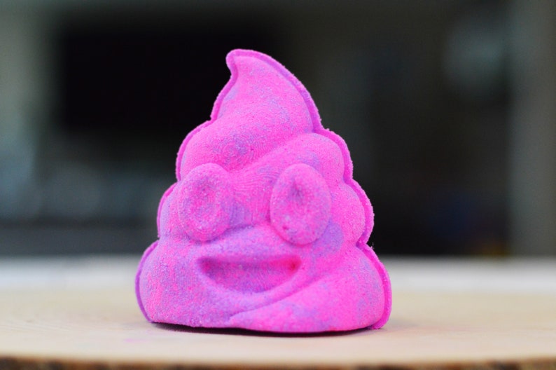 Puede incluir: Una bomba de ba&ntilde;o rosa y morada con forma de emoji de caca sonriente.
