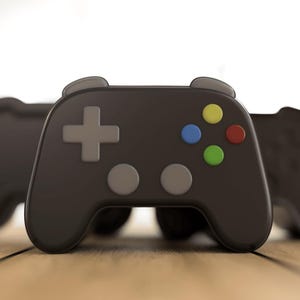 May include: Three black game controllers with grey buttons and directional pads are arranged on a wooden surface. The controllers have coloured buttons in yellow, blue, green, and red. The background is blurred.