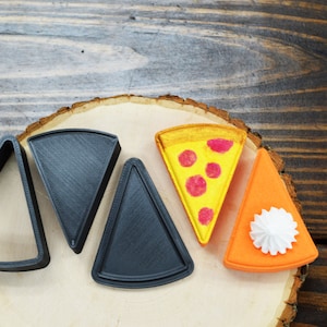 May include: Five different shaped cookie cutters, three are black and two are colored. The colored cutters are a yellow and orange pizza slice and an orange pumpkin pie slice.