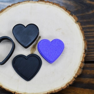 May include: Four heart-shaped objects, three are black and one is purple, on a wooden surface.