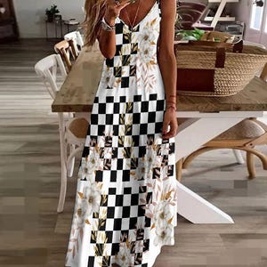 May include: A sleeveless maxi dress featuring a V-neckline and a black and white checkered pattern. The dress is adorned with floral and leaf accents in white, gold, and brown. The dress has a flowing, tiered design.
