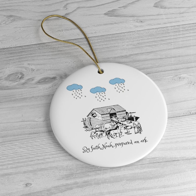 May include: A white ceramic ornament with a black and white illustration of Noah's Ark with animals and people boarding the ark. Three blue clouds with rain are above the ark. The text "By faith Noah prepared an ark" is written below the ark.