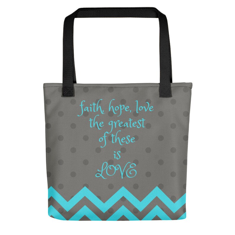 K&ouml;nnte beinhalten: Eine graue und t&uuml;rkisfarbene Einkaufstasche mit einem Zickzackmuster am Boden und Punkten oben. Die Tasche hat schwarze Henkel und den Text "faith hope, love the greatest of these is LOVE" in T&uuml;rkis.