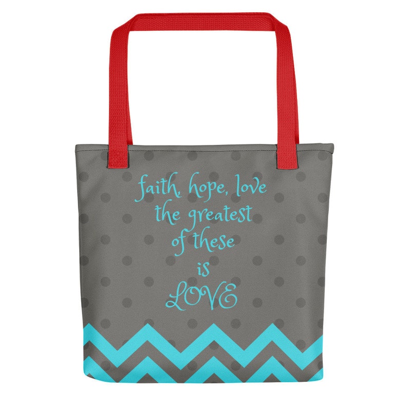 K&ouml;nnte beinhalten: Eine graue Tragetasche mit roten Henkeln und einem blauen Zickzackmuster am Boden. Die Tasche hat wei&szlig;e Punkte und den Text "faith hope, love the greatest of these is LOVE" in blau.