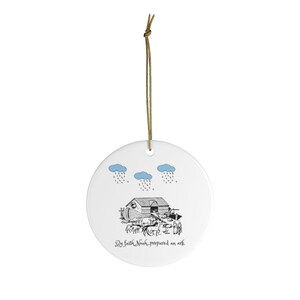 May include: A white ceramic ornament with a black and white illustration of Noah's Ark with animals and people. The text "By faith Noah prepared an ark" is written below the ark. There are three blue clouds with rain drops above the ark.