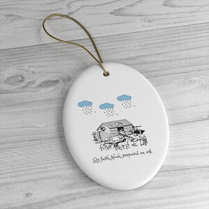 May include: White oval ceramic ornament with a black and white illustration of Noah's Ark with animals and people. The text "By faith, Noah prepared an ark" is written below the ark. Three blue clouds with rain are above the ark.