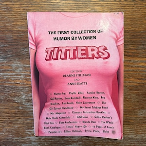 May include: A pink book cover with the title "TITTERS" in red letters. The cover features a graphic of a pink t-shirt with the text "THE FIRST COLLECTION OF HUMOR BY WOMEN". The book is edited by Deanne Stillman and Anne Beatts.