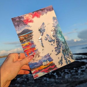 May include: A rectangular art print featuring a stylized map of the Outer Hebrides in Scotland. The artwork uses vibrant watercolor textures in shades of blue, purple, orange, and red, depicting a small white cottage and a mountain landscape.