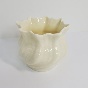 May include: A white ceramic vase with a ruffled rim and a textured surface.