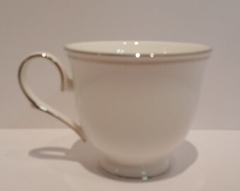 May include: A white teacup with a gold rim and a handle. The cup is sitting on a white surface.