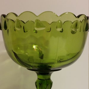 May include: A green glass pedestal bowl with a scalloped rim and a fluted stem. The bowl is perfect for serving fruit, candy, or other treats.