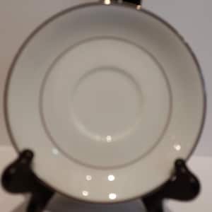 Puede incluir: Plato de porcelana blanco con un fino borde dorado. El plato está sobre un soporte negro.