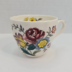 Puede incluir: Una taza de té blanca con un patrón floral. El patrón presenta flores rosas, amarillas y azules sobre un fondo blanco.