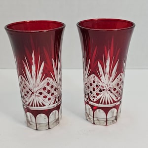 Puede incluir: Dos vasos de chupito de vidrio rojo con un diseño de corte claro. Los vasos tienen una parte superior acampanada y una base redonda.