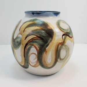 Könnte beinhalten: Eine weiße Keramikvase mit rundem Körper und blauem Rand. Die Vase ist mit abstrakten Wirbeln in Braun-, Grün- und Gelbtönen verziert.