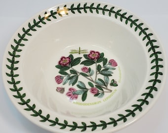 May include: White ceramic bowl with a green and gold border. The bowl features a botanical illustration of a Rhododendron Lepidota plant with pink flowers and green leaves. The text "RHODODENDRON LEPIDOTUM" is printed on the bowl.