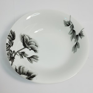 Puede incluir: Tazón de cerámica blanco con un diseño floral en blanco y negro. El diseño presenta una flor grande y hojas.