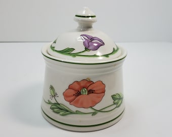 May include: White ceramic sugar bowl with a lid, featuring a floral design with red, pink, and green flowers. The bowl has a green trim around the top and bottom.