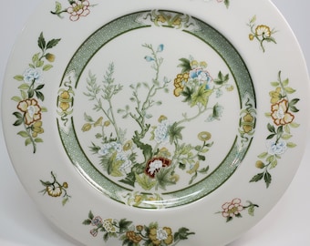 Puede incluir: Un plato de cena de cerámica blanca con un diseño floral verde y blanco. El plato tiene un borde elevado y un borde festoneado.