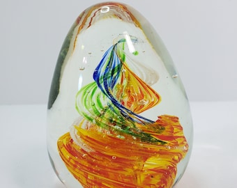 Könnte beinhalten: Ein durchsichtiger Glas-Papiergewicht mit einem wirbelnden Design aus orangefarbenem, gelbem, grünem und blauem Glas.