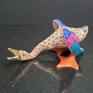 May include: A porcelain goose figurine with a red, white, and blue patterned design. The goose is lying on its side with its wings spread out. The figurine is hand-painted and has a glossy finish.