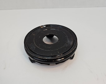 May include: A black round wooden plant stand with a circular opening in the center and three legs.