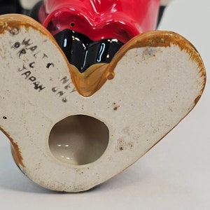 May include: The base of a ceramic figurine with a red face and black eyes. The figurine is marked "Walt Disney" and "Made in Japan".