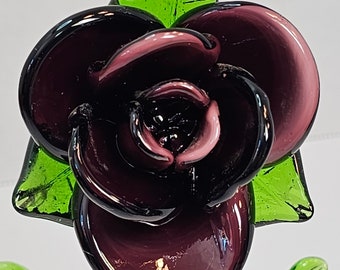 May include: A glass rose with a dark purple and pink flower and green leaves.