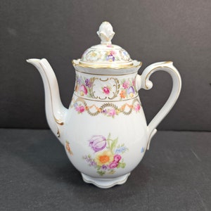 May include: White porcelain teapot with a floral design in shades of pink, purple, yellow, and blue. The teapot has a gold trim and a lid with a knob.