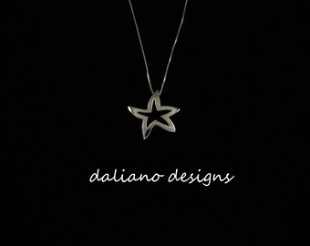 May include: A silver necklace with a delicate, openwork star pendant. The pendant is a simple, modern design with a smooth, polished finish. The necklace is on a black background.
