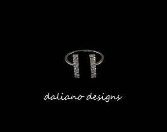 May include: A silver ring with two vertical rows of clear cubic zirconia stones. The ring is open on one side and has a simple, minimalist design. "daliano designs" is written in white text below the ring.