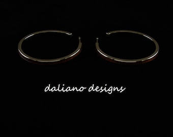 May include: A pair of silver hoop earrings with a thin wooden inlay. The earrings are on a black background.