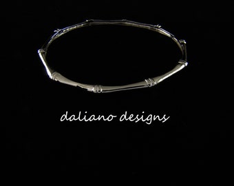 May include: A silver-toned necklace with a bamboo-like design, featuring segmented sections and rounded connectors. The necklace is displayed against a black background, with the text "daliano designs" in a cursive font.