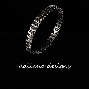 May include: A silver bangle bracelet with a leaf design. The bracelet is made of metal and has a smooth finish.
