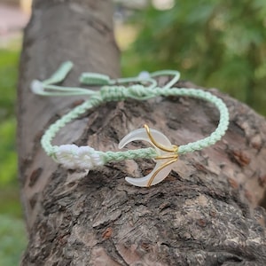 May include: A green and white braided bracelet with a white crescent moon charm wrapped in gold wire.