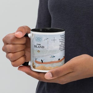 May include: A ceramic mug with a black interior and handle, featuring a graphic design of Fire Island, New York. The print includes the text 'NY FIRE ISLAND', a compass rose, a lighthouse, a boat, a deer, a person fishing, and descriptive text.