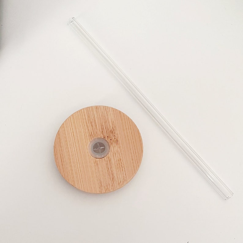 May include: A bamboo lid with a clear plastic straw and a clear plastic stopper. The lid is round and made of light brown bamboo. The straw is straight and transparent. The stopper is in the centre of the lid.
