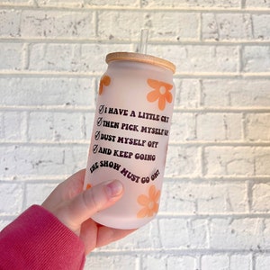 May include: A frosted glass tumbler with a bamboo lid and a straw. The tumbler has a floral design and the text "I have a little cry, then pick myself up, dust myself off, and keep going. The show must go on!"